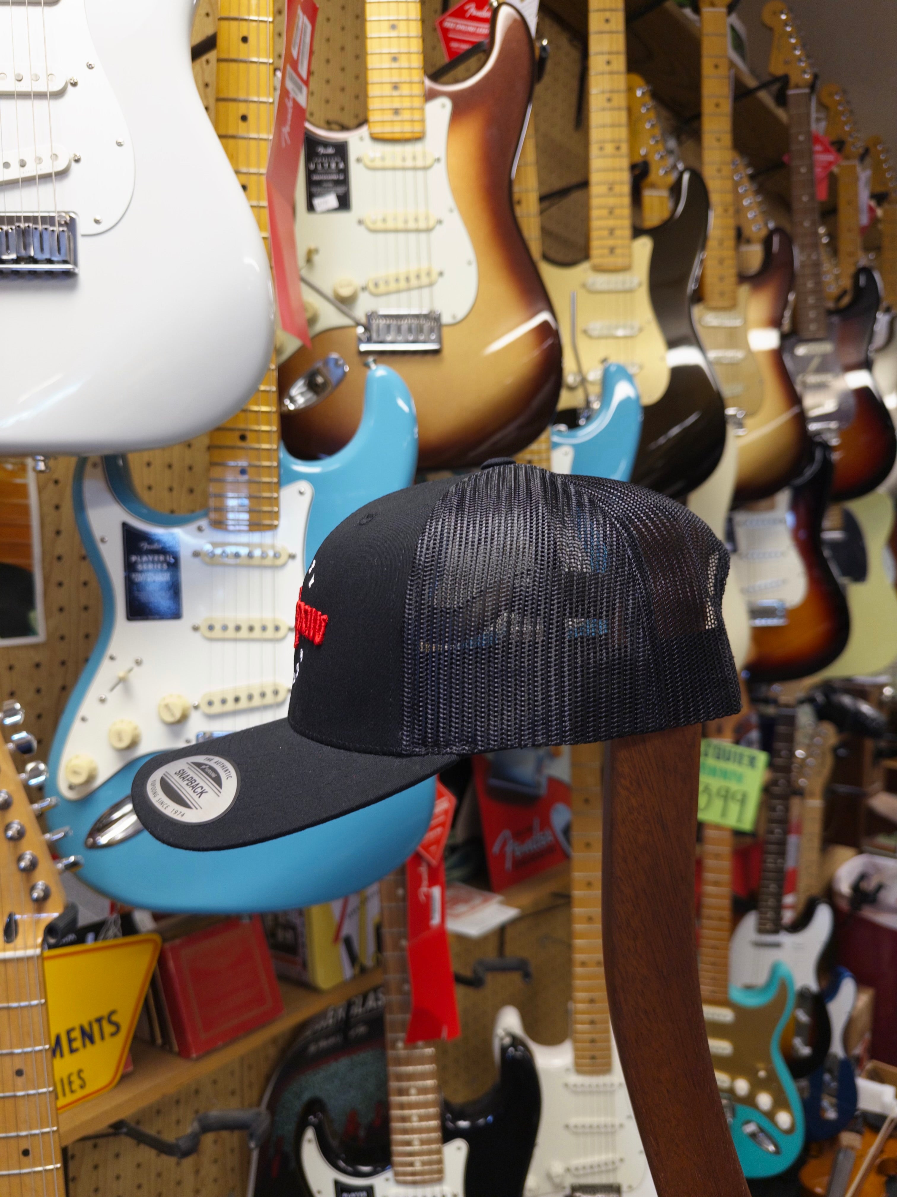 Black cap with red logo hanging among guitars in a store