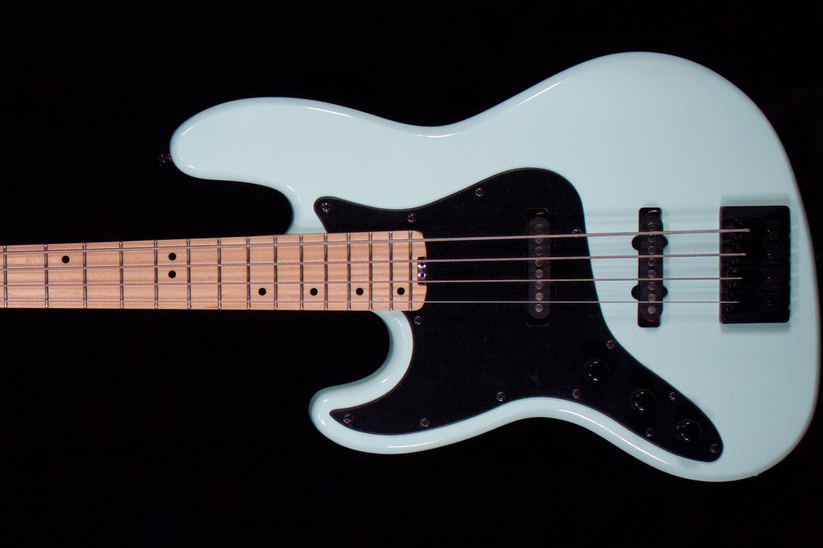 A close-up of a white electric bass guitar against a solid black background, showing the body, pickguard, bridge, and part of the neck.